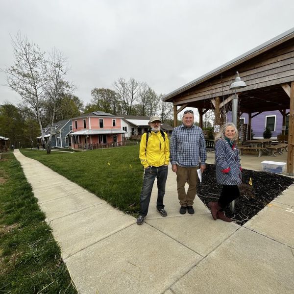 Three people standing outside a cohousing community with colorful houses in the background.