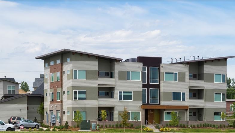 Modern multi-story apartment building in a suburban setting with green landscaping.