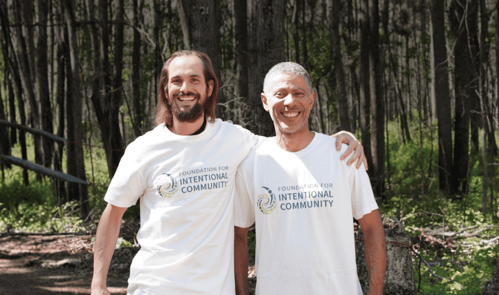 Two smiling men in white Foundation for Intentional Community t-shirts outdoors.