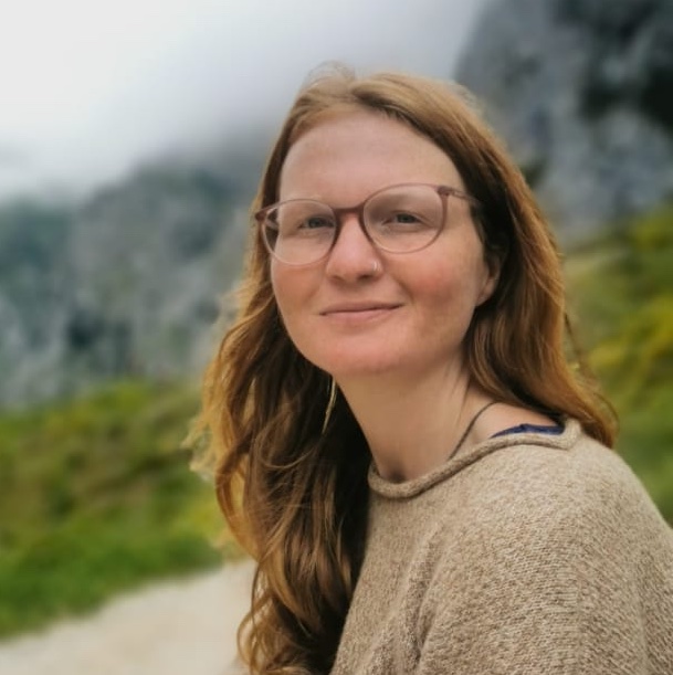 Woman with glasses outdoors in a natural setting for community building.