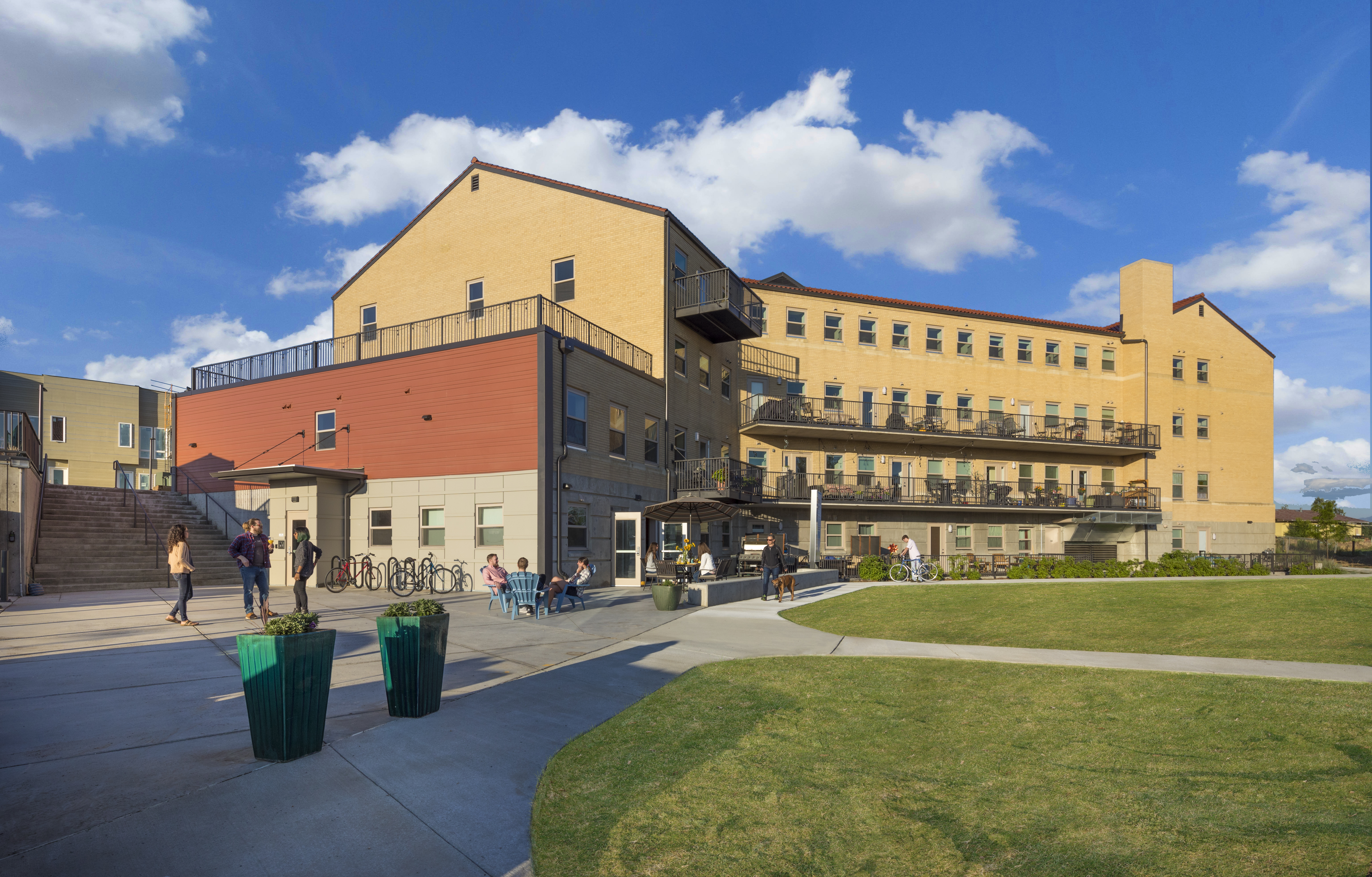Modern cohousing community building with outdoor gathering space and green lawn.