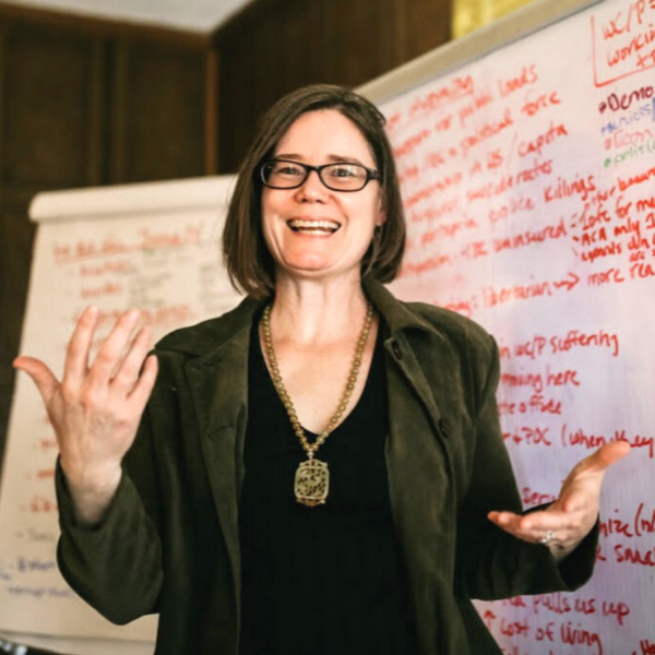 Woman speaking at Foundation for Intentional Community event with whiteboard in background.