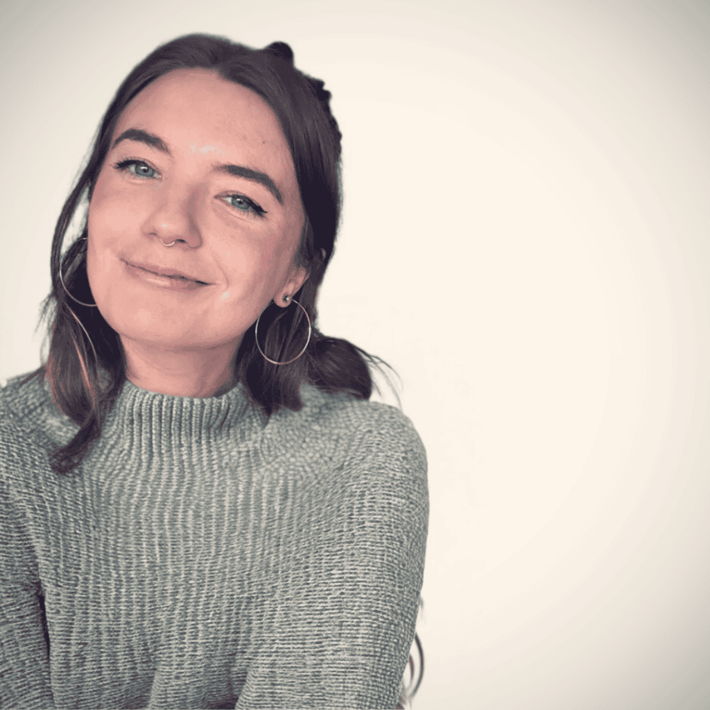 Young woman with long brown hair and a friendly smile, wearing a gray sweater.